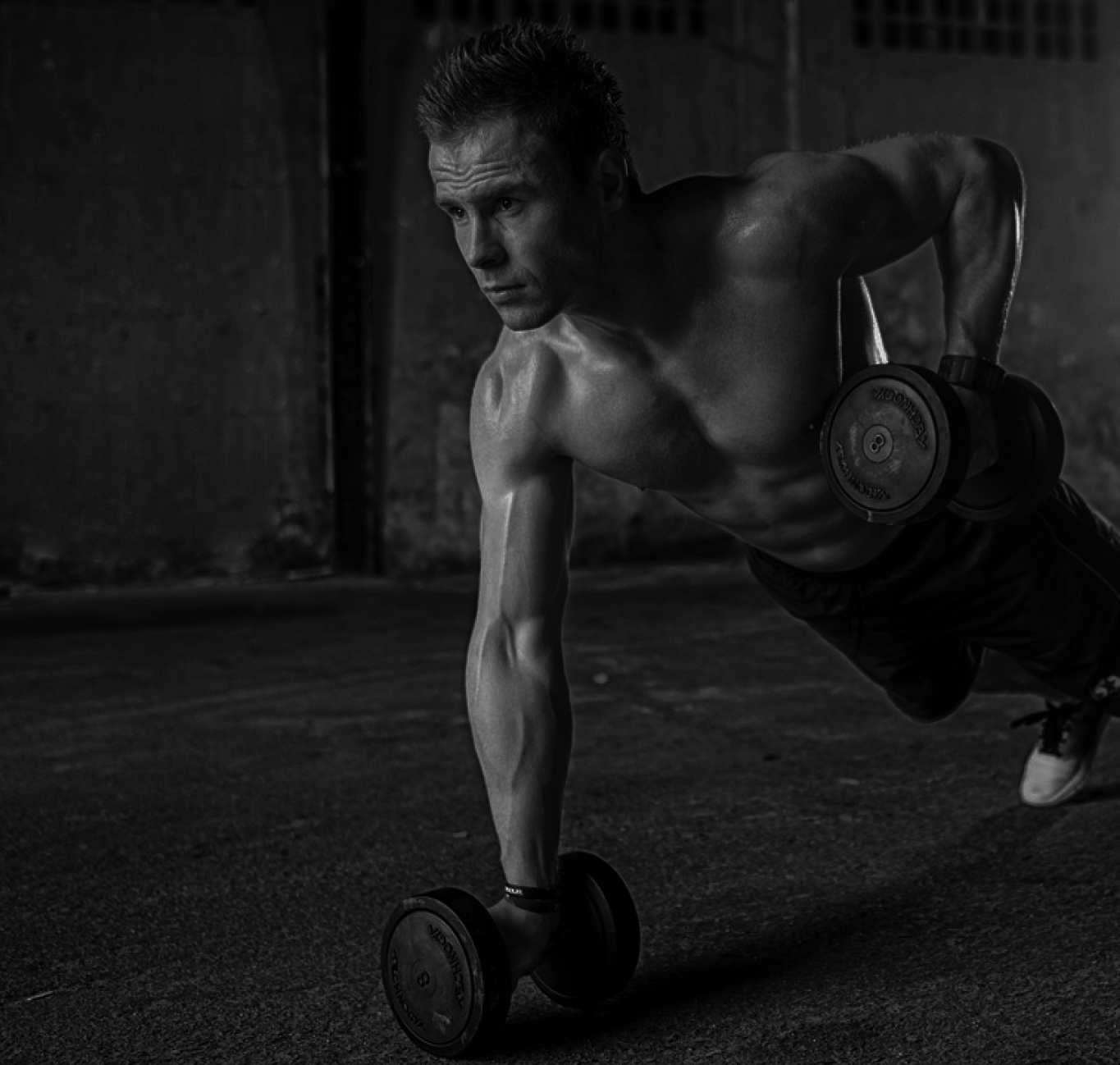 Gray scale image of man training with dumbbells, doing push-ups